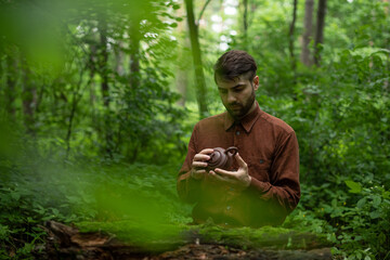 Man holding clay teapot near wooden log in forest at background 