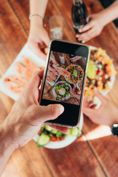 Vertical photo of last generation mobile taking a photo of the food that is on a wooden table with friends sharing the food