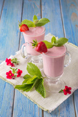 strawberry yogurt in a glass cup on a blue wooden table.
