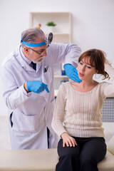 Naklejka premium Young woman visiting old male doctor otorhinolaryngologist