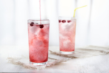 Two glasses of cold pink lemonade with blackcurrant berries on a white background in a blur.