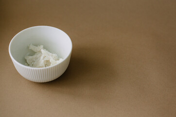 White bowl with coconut paste on a brown background. Minimalistic food design.