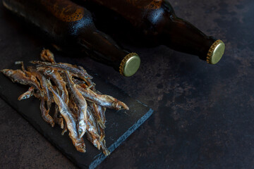 Two Bottles of beer with dried smelt fish  on dark stone background