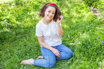 Naklejka na ściany i meble Happy girl smiling outdoor. Beautiful young brunete woman with brown hair resting on park or garden green grass background. European woman. Positive human emotion facial expression body language.