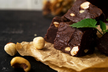 Fondant on craft crumpled paper with nuts and chocolate cubes decorated with green mint leaves. In the background a jar of nuts, blurred background. 