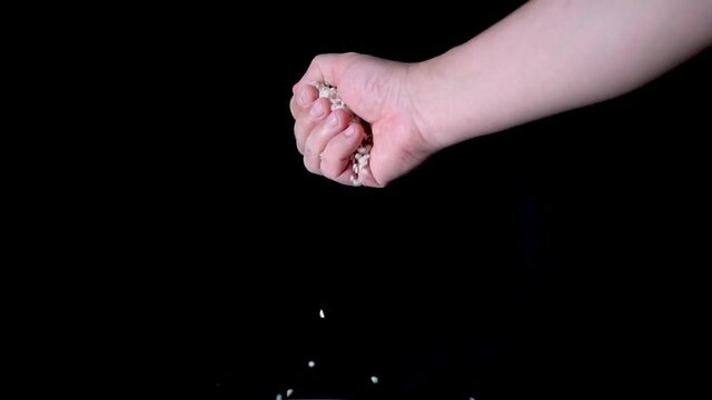 Hand of a man making rice grains, with black background, in slow motion.
