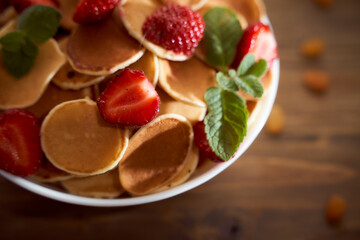 Mini pancakes with strawberries, nuts, mint, orange on a dark brown wooden table. closeup. With copy space