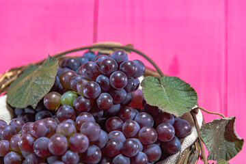 Bunch of grape in wicker basket on pink background
