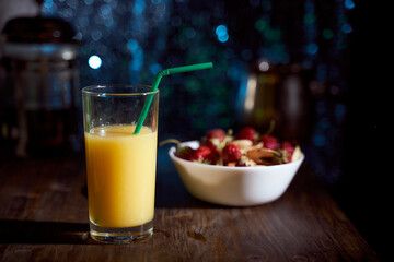 orange juice in a high glass with a green tube and berries on a dark blue bokeh background. With copy space