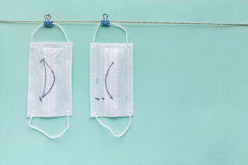 Medical masks hanging on a clothesline on green paper background. Smiling and crying mask.