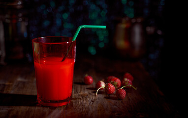 milkshake in a bright red glass with strawberries on a wooden table. Dark blue bokeh background. With copy space