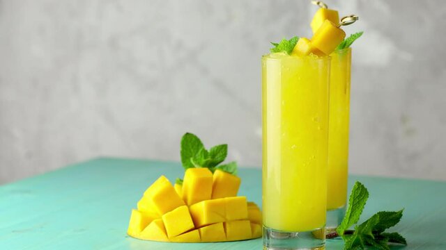 Fresh summer ice cold mango cocktail with mint  and mango fruit. Fresh mango juice moving slowly on light blue background