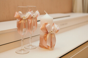 wedding attributes such as glasses and a candle decorated with pink ribbons with large bows are on the table
