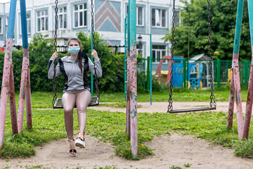 girl on the playground in a medical mask. Girl in a medical mask on a swing