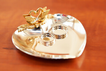 Gold wedding rings lie on a shiny stand similar to a saucer