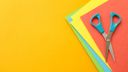 blue open scissor on colorful sheets paper on orange bacground. Concept crafts, handmade origami, decorative. Flatlay, copyspace