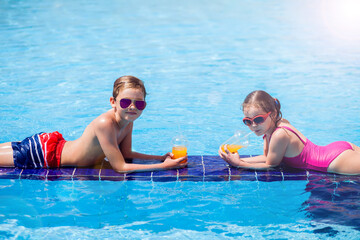 Kids boy and girl holding juice in the swimming pool. Childhood, summer and vacation concept