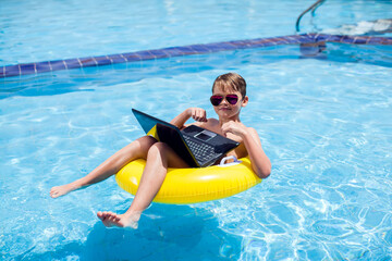 Kid boy using laptop in the swimming pool. Technology, summer and vacation concept