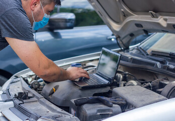 auto mechanic with protective mask diagnosing car with black laptop