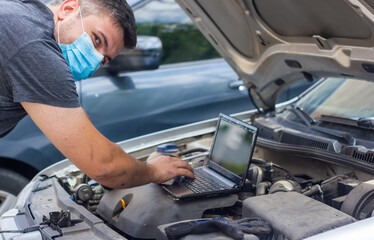 auto mechanic with protective mask diagnosing car with black laptop