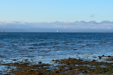 fog shrouded mountain range and fishing vessel on fjord in the distance