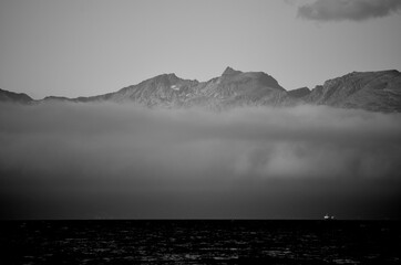 Fototapeta na wymiar fog shrouded mountain range behind fjord and fishing boats