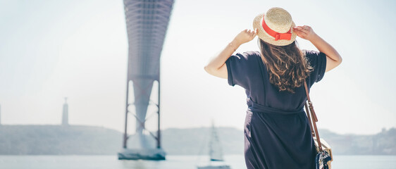 The girl looks at the bridge called April 25 in Lisbon in Portugal in sunny summer day. View from...