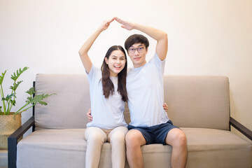 a couple wearing blue shirt is sitting on a sofa and making arms roof at home © tonefotografia