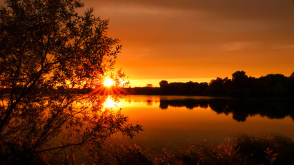 Symmetry of the sky in a lake at sunrise. Clouds reflecting on the water. Holiday landscape by the sea. Quiet relaxing scene with a beautiful colorful sky. Vegetation in the foreground.