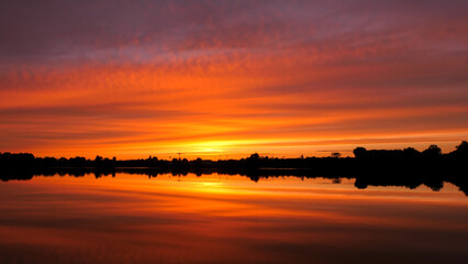 Symmetry of the sky in a lake at sunrise. Clouds reflecting on the water. Holiday landscape by the sea. Quiet relaxing scene with a beautiful colorful sky.