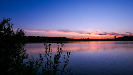 Symmetry of the sky in a lake at sunrise. Clouds reflecting on the water. Holiday landscape by the sea. Quiet relaxing scene with a beautiful colorful sky. Vegetation in the foreground.