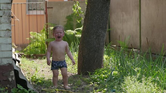 Naked boy is crying hysterics wet toddler 2 years old in backyard slow motion