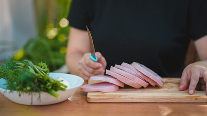 Young woman cutting sausage on wooden board outdoors. Women's hands cutting sausage goods with knife on chopping board.
