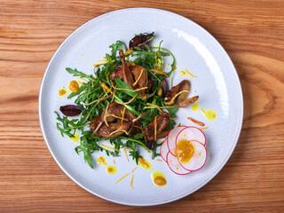 Fried quails on arugula salad with fried potato chips on a white plate on a wooden background