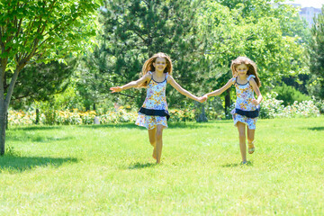 Naklejka na ściany i meble Two girls holding hands run on a green lawn in a park