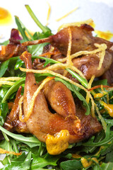 Fried quails on arugula salad with fried potato chips on a white plate on a wooden background