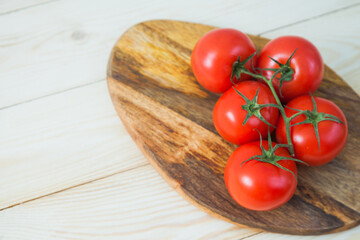 Fresh juicy tomato branch on wooden plate. Red vegetable on table. Vegetarian food, tasty product concept.