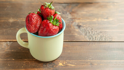 ripe fragrant strawberries in a ceramic mug on a wooden table