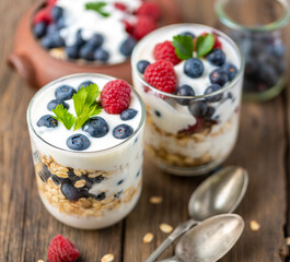 White yogurt in two bowls with blueberries, raspberries on natural wooden desk.