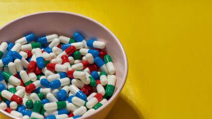 Creative concept with different medical pills, capsules lying in bowl isolated on yellow background. Health care and treatment concept