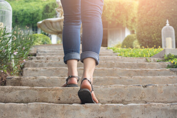 Young adult woman walking up the stairs in the garden with sun sport background, woman climbing stone steps  in the garden to success.