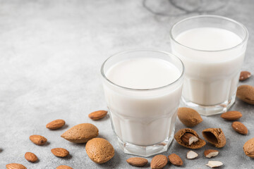 Plant based almond vegan milk in glasses with nuts on concrete background. Dairy free milk