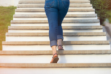 Young adult woman walking up the stairs in the garden with sun sport background, woman climbing...