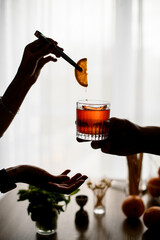 man's hand holds glass with cocktail while woman s hand carefully decorates it