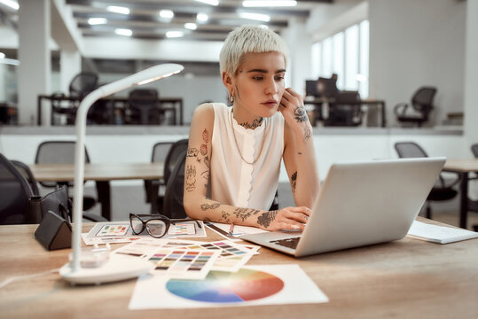 Creative occupation. Young stylish tattooed female designer working on new project while standing near office desk
