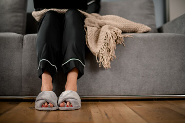 front view on legs of woman in black silk pajama and grey slippers