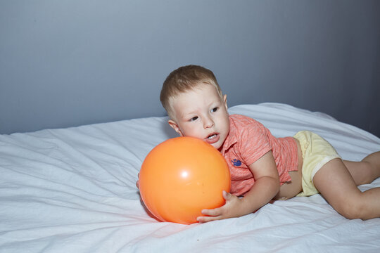 Two Year Old Kid Playing With A Ball On A Gray Background