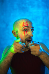 Stylish bald man points fingers at camera. Fluorescent paint in neon light. Way to meet in nightclub or party.