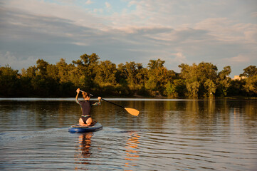 Rear view of woman which sits on sup board holds paddle and floats on the river