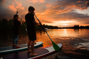 two people standing on sup boards and going to swim on the river at sunset